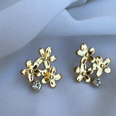 Brincos dourados em forma de flores com pedras brilhantes sobre tecido branco