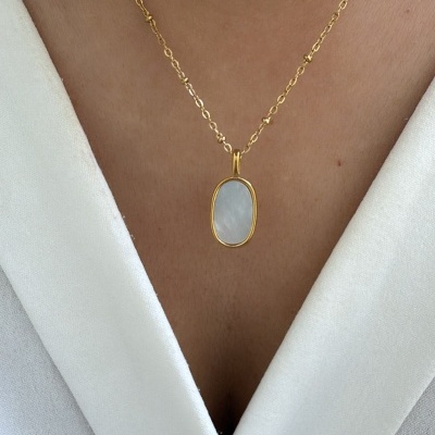 Colar dourado com pendente oval branco usado com blusa branca
