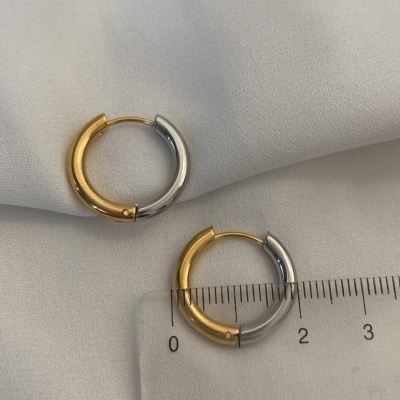 Brincos de argola bicolor dourado e prateado sobre tecido branco com régua