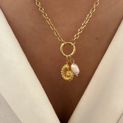 Colar dourado com pingente de flor e pérola em pele morena e roupa bege clara