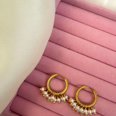 Brincos dourados com bolas brancas numa almofada rosa