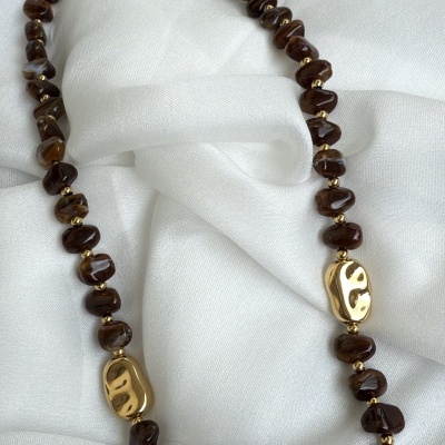 Colar de pedras castanho-escuro e contas douradas sobre tecido branco