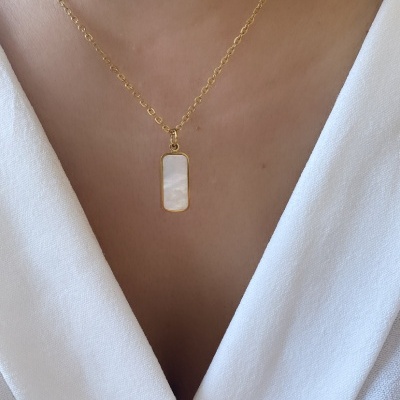 Colar dourado com pendente retangular de madrepérola em pescoço sobre roupa branca