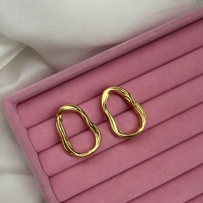 Brincos dourados com textura ondulada em caixa rosa sobre tecido branco