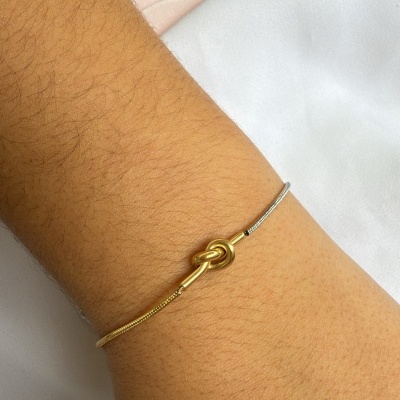 Pulseira fina dourada e prateada com nó dourado no pulso