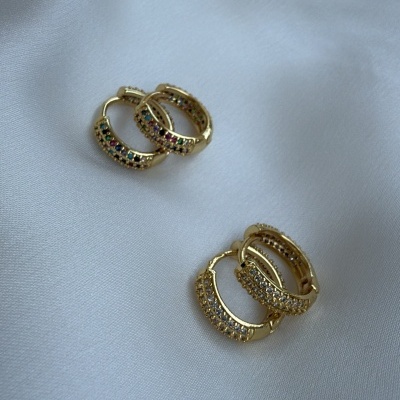 Dois pares de brincos argola dourados com pedras coloridas e brancas sobre tecido branco.