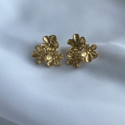 Brincos dourados em forma de flores sobre tecido branco