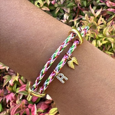 Pulseira trançada colorida com detalhes dourados e pendentes numa mão