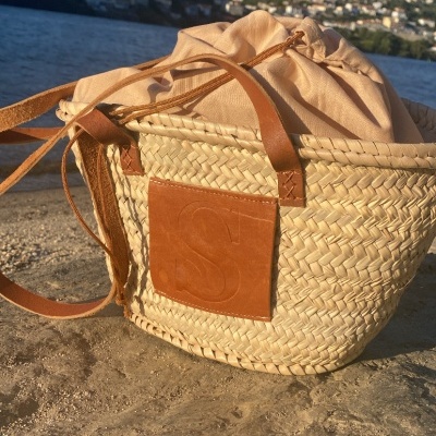 Mala de senhora trançada com bolso de couro e saco bege ao lado da água