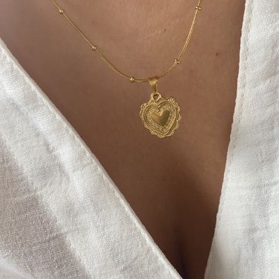 Colar dourado com pendente de coração em corrente fina sobre pele e camisa branca