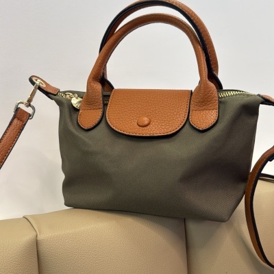 Mala de mão pequena castanha e verde com asas de couro castanho sobre sofá bege