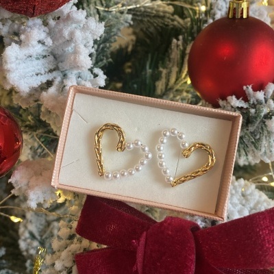 Brinco de coração dourado com pérolas em caixa sobre árvore de Natal decorada