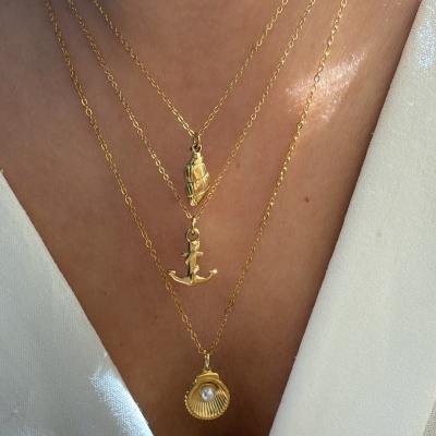 Três colares dourados com pendentes diversos em pescoço sobre blusa branca