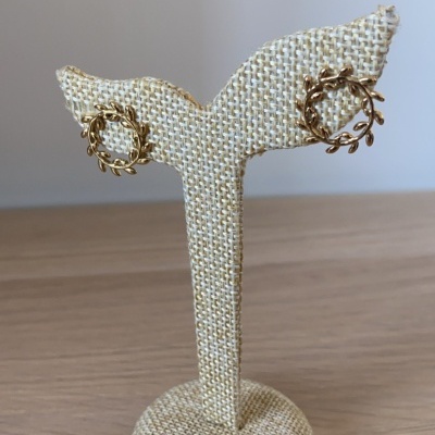 Brincos dourados com padrão de raminhos em suporte bege e fundo cinzento