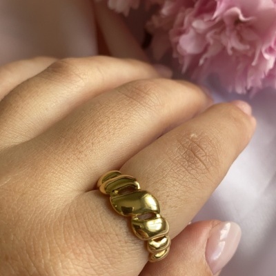 anel dourado ondulado em dedo com flores cor-de-rosa ao fundo