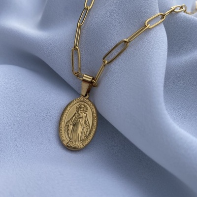 Colar dourado com pendente oval religioso sobre tecido azul claro