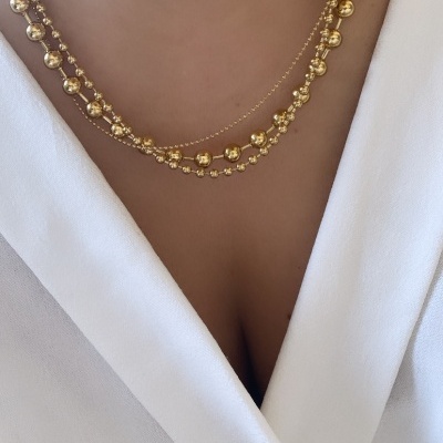 Colar dourado com bolas metálicas em três fios sobre blusa branca com decote em V