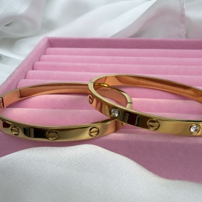 Braceletes dourados com parafusos e pedras em estojo rosa.