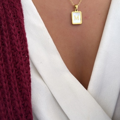 Colar dourado com pendente retangular branco e letra M