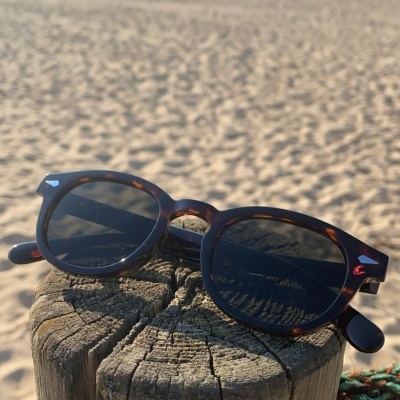 Óculos de sol com armação tartaruga sobre poste de madeira na praia