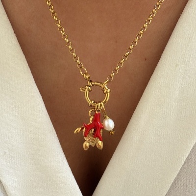 Colar dourado com pendente vermelho e pérola numa pessoa com camisa bege clara