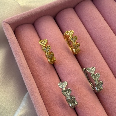 Brincos dourados e prateados com corações e pedras em caixa de veludo rosa