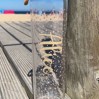 Garrafa de vidro transparente com tampa de madeira e alça junto à praia