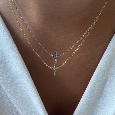 Dois colares com cruzes douradas e prateadas penduradas no pescoço de uma pessoa com roupa branca