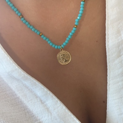 Colar azul com contas e pendente dourado num pescoço com camisa branca