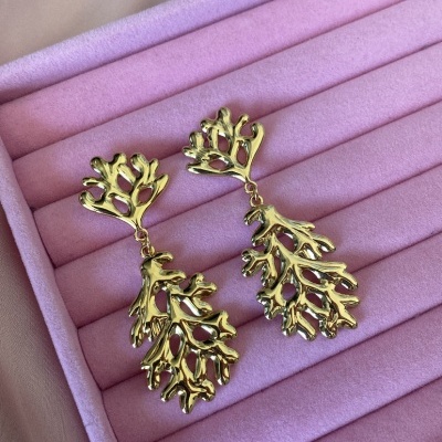Brincos dourados com design de ramos sobre almofada rosa