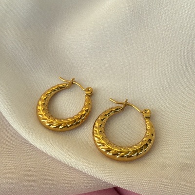 Brincos de argola dourados texturizados sobre tecidos branco e rosa