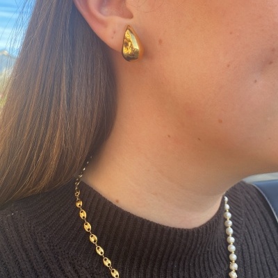 Brincos dourados irregulares e colar de pérolas com corrente dourada em mulher com camisola preta