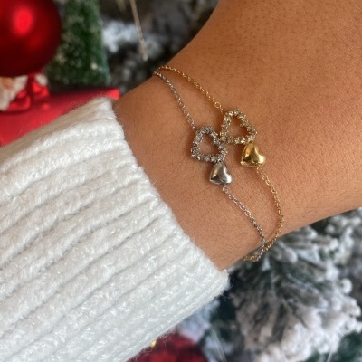 Pulso com pulseiras dourada e prateada com corações e árvore de Natal decorada ao fundo