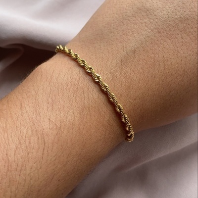 Pulseira dourada fina com design torcido no pulso