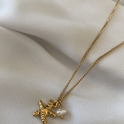 Colar dourado com pendente figura humana e pérola sobre tecido branco