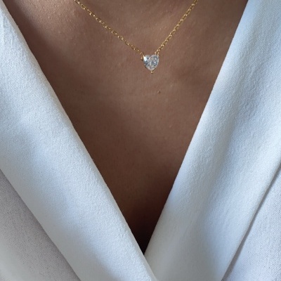 Colar dourado com pendente de coração brilhante sobre blusa branca