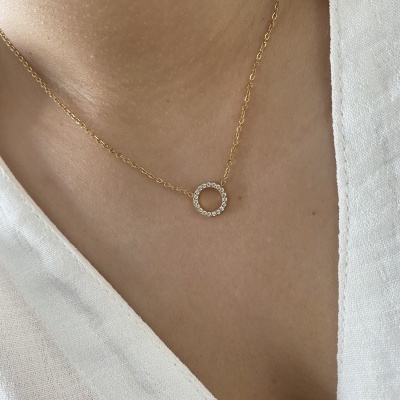 Colar dourado com pendente circular de cristais num pescoço com camisa branca