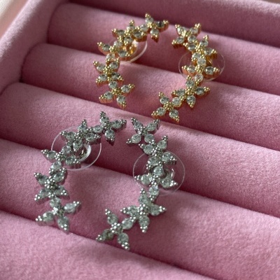 Dois pares de brincos meia-lua dourados e prateados com flores e pedras em caixa rosa.