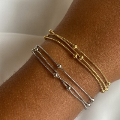 Pulseiras finas douradas e prateadas com bolas metálicas no pulso.
