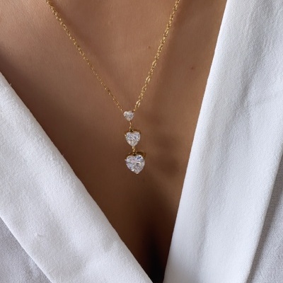 Colar dourado com três corações brilhantes sobre roupa branca