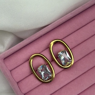 Brincos dourados ovais com pedras transparentes em caixa rosa.
