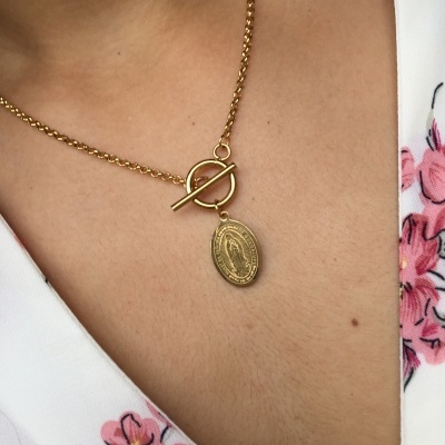 Colar dourado com pendente de medalha religiosa em corpo com vestido branco floral