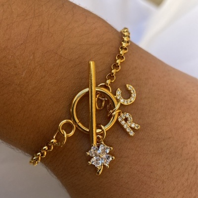 Pulseira dourada com letras C e R em pedras brilhantes num pulso.