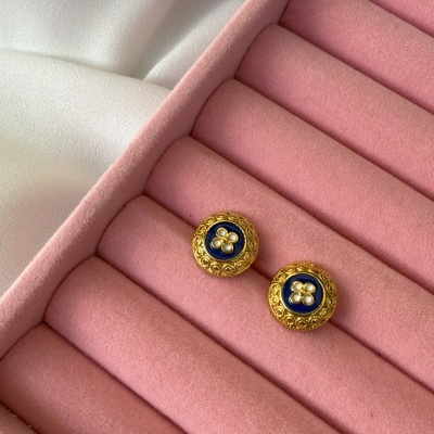 Par de botões dourados com interior azul e detalhe floral branco numa caixa rosa aveludada