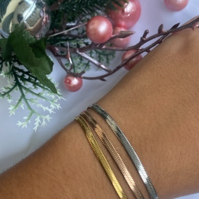 Pulseiras finas dourada, rosé e prateada no pulso com decoração floral ao fundo