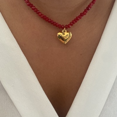 Colar vermelho com pendente coração dourado no pescoço de mulher com roupa branca