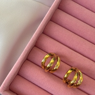 Brincos dourados em caixa de veludo rosa sobre tecido branco