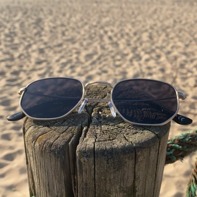 Óculos de sol de armação metal prateada sobre poste de madeira numa praia