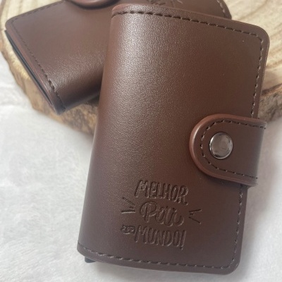 Carteiras castanhas em pele sintética com fecho metálico, uma gravada com 'MELHOR PAI DO MUNDO!'.