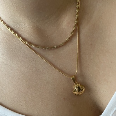 Colar dourado com pendente de concha sobre pele e camiseta branca